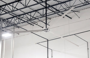 DDI HVLS Industrial Ceiling fan in a warehouse setting with high ceilings and metal beams.