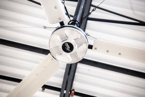 DDI HVLS Industrial Ceiling fan with silver blades and motor installed on a corrugated metal ceiling.